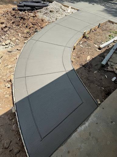 Curved concrete walkway with a dark paver border under construction.